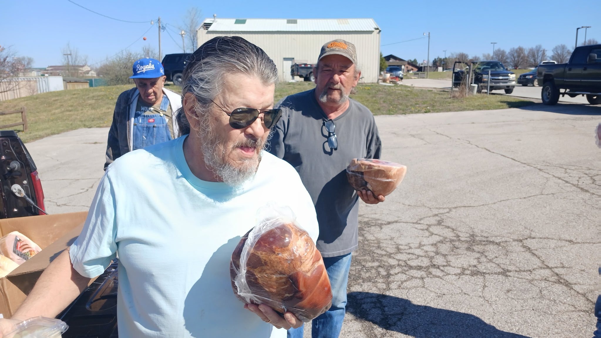 Men holding smoked hams at outdoor food distribution