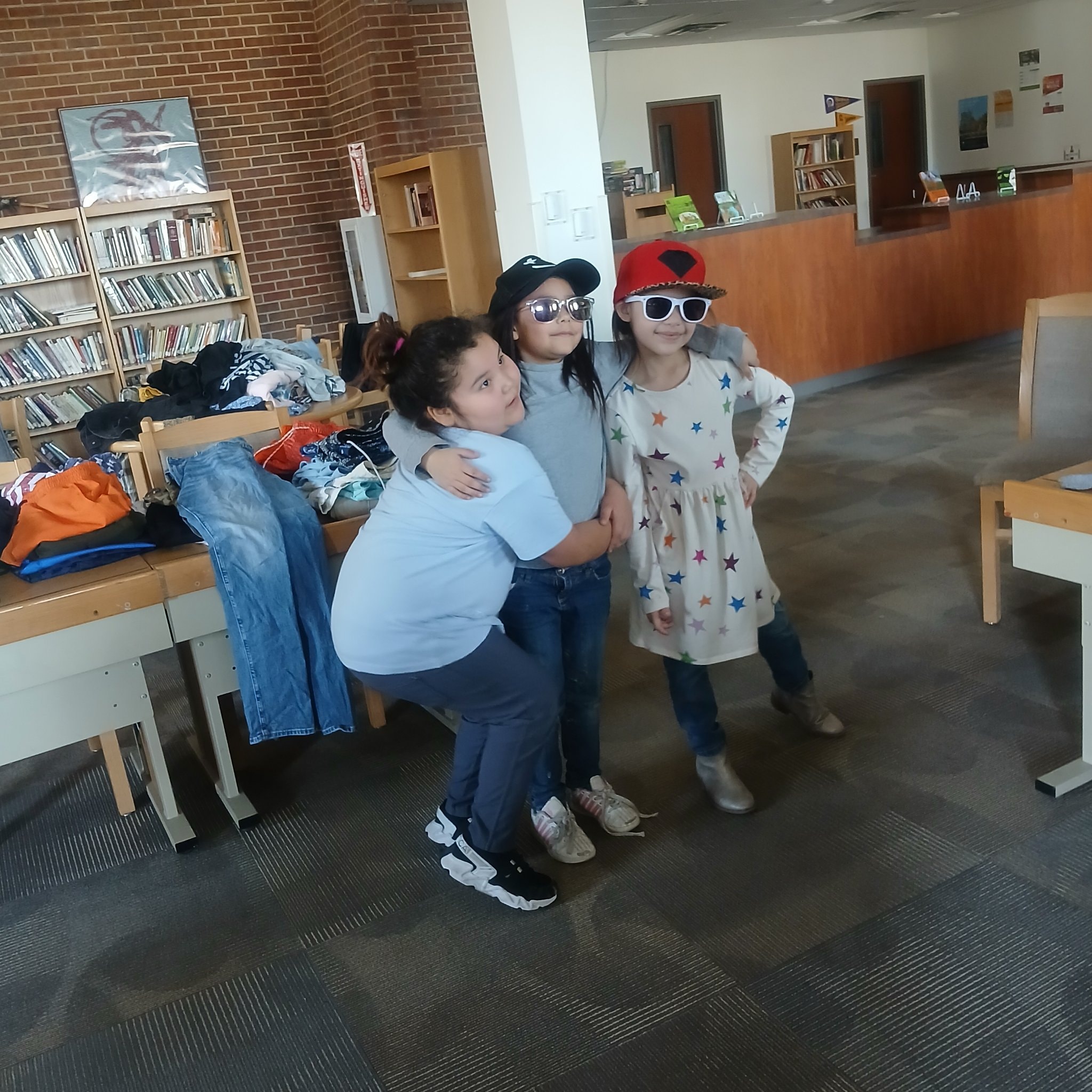 Three kids wearing sunglasses and hats at clothing donation event in library
