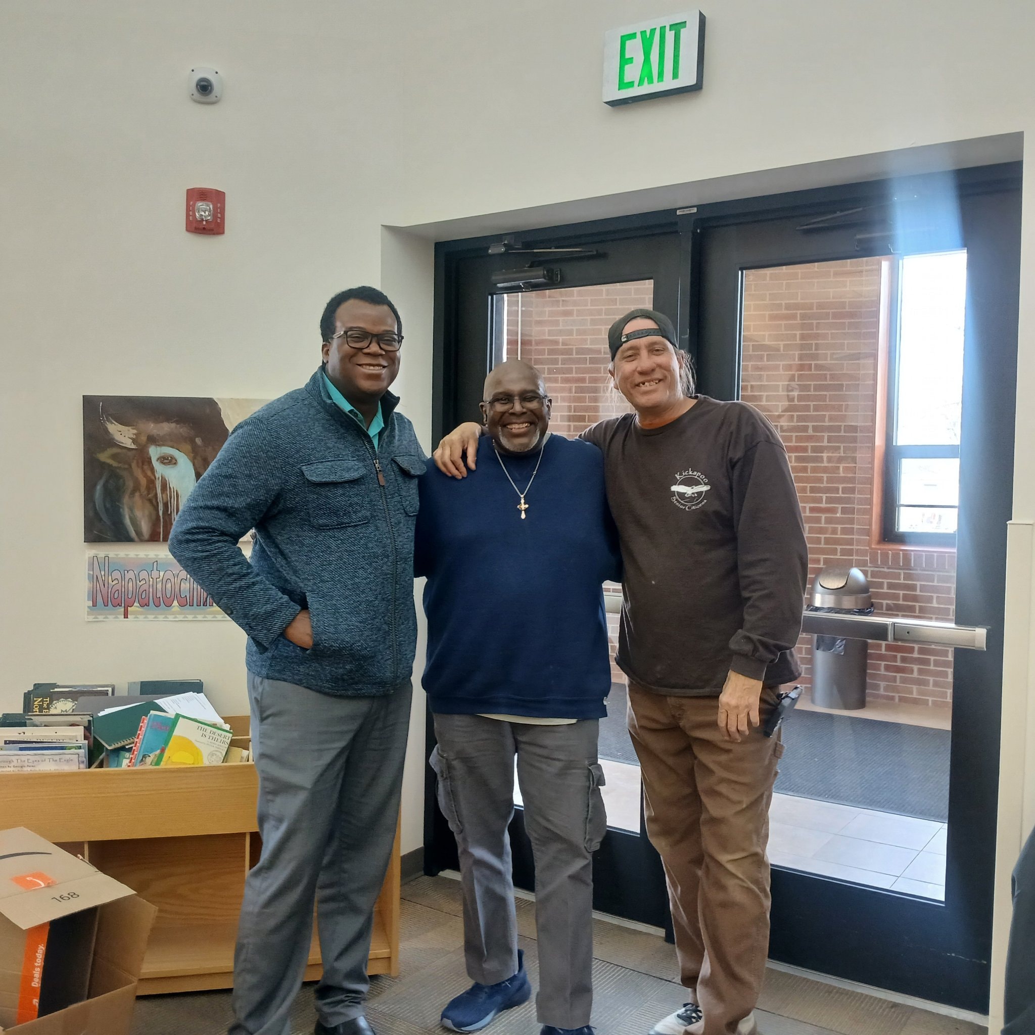 Three men posing together indoors by exit doors